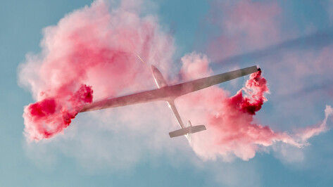 Segelflugzeug SZD-59-1 Acro bei Flugshow mit rotem Rauch vor blauem Himmel.